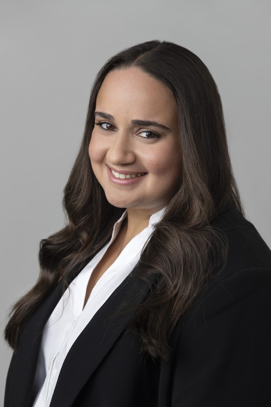 Smiling headshot of a professional female therapist wearing a black blazer and white shirt, posed against a neutral gray background—representing Making Meaning Psychology, a warm and approachable mental health practice in New York.